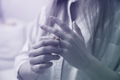 Image of Woman taking off wedding ring indoors, closeup. Cheating and breakup