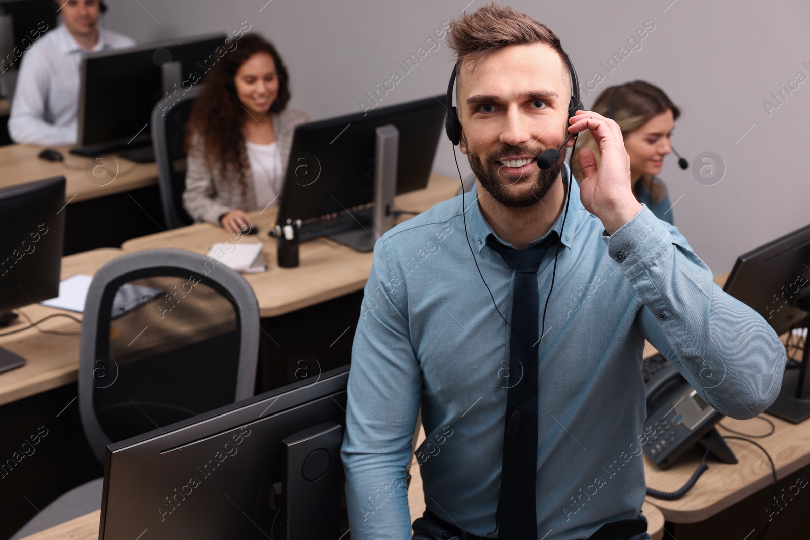 Photo of Handsome call center operator with headset and his colleagues working in office, above view