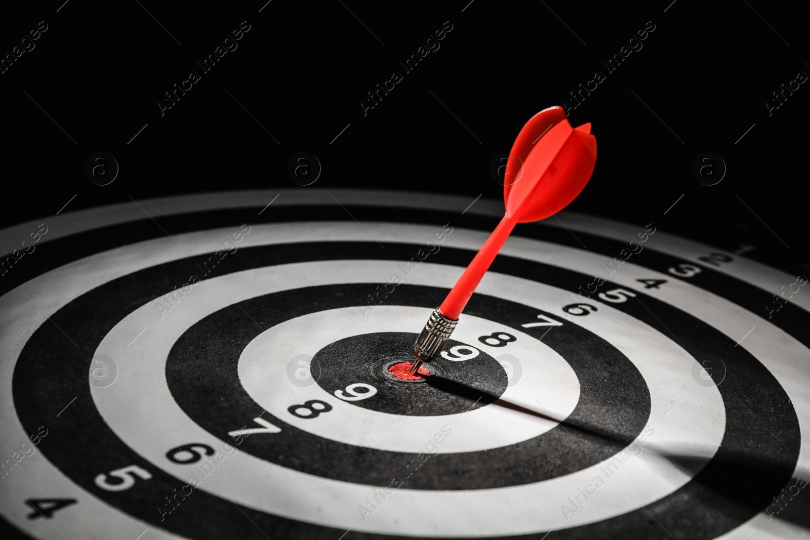 Photo of Red arrow hitting target on dart board against black background