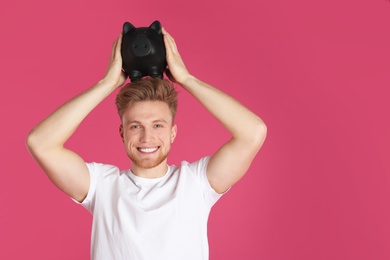 Photo of Young man with piggy bank on color background, space for text. Money saving