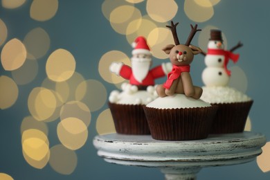 Photo of Tasty Christmas cupcakes on dessert stand against blurred festive lights, space for text