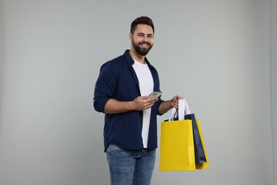 Happy man with many paper shopping bags and smartphone on grey background