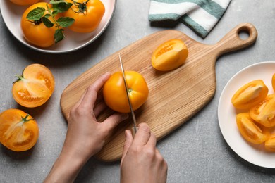 Photo of Woman cutting fresh ripe yellow tomato at light grey table, top view