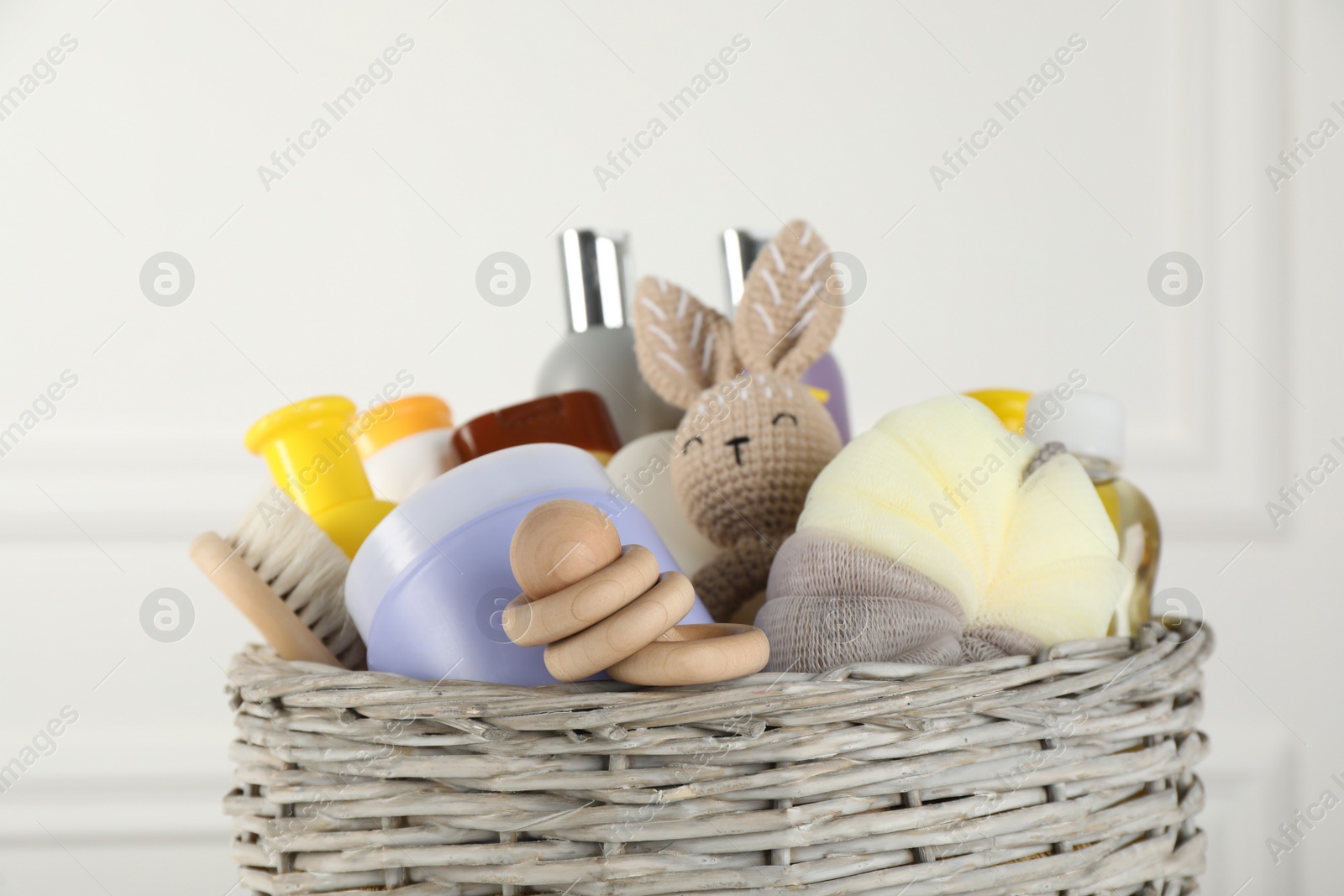 Photo of Wicker basket full of different baby cosmetic products, accessories and toys on blurred background, closeup