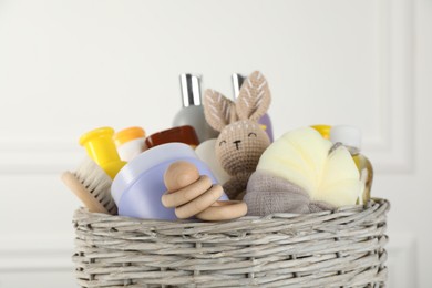 Photo of Wicker basket full of different baby cosmetic products, accessories and toys on blurred background, closeup