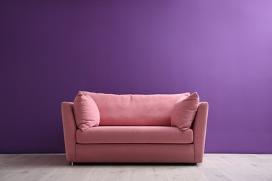 Comfortable pink sofa near purple wall in living room interior. Space for text
