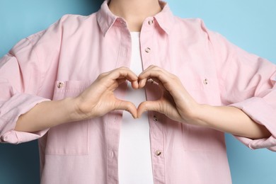 Photo of Woman making heart with hands on light blue background, closeup