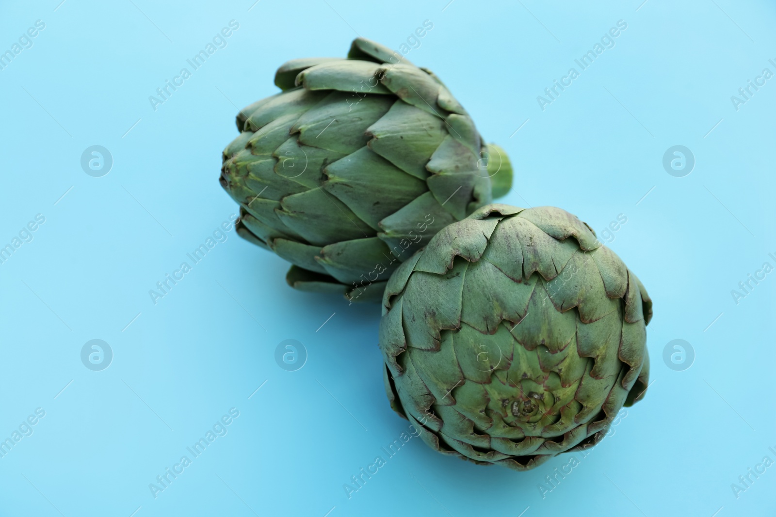 Photo of Whole fresh raw artichokes on light blue background, closeup