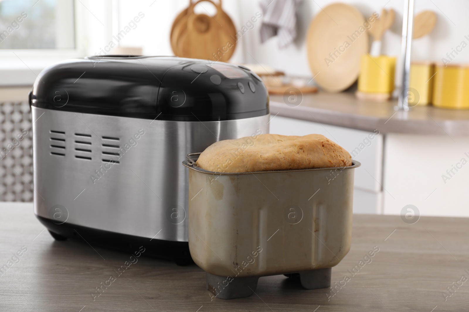 Photo of Breadmaker and fresh homemade bread in pan on wooden table in kitchen