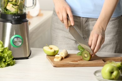 Photo of Woman preparing ingredients for tasty green smoothie at white wooden table in kitchen, closeup