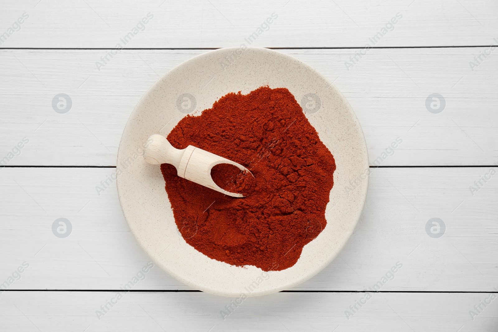 Photo of Plate of aromatic paprika on white wooden table, top view