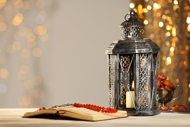 Arabic lantern, Quran, misbaha and dates on table against blurred lights, space for text