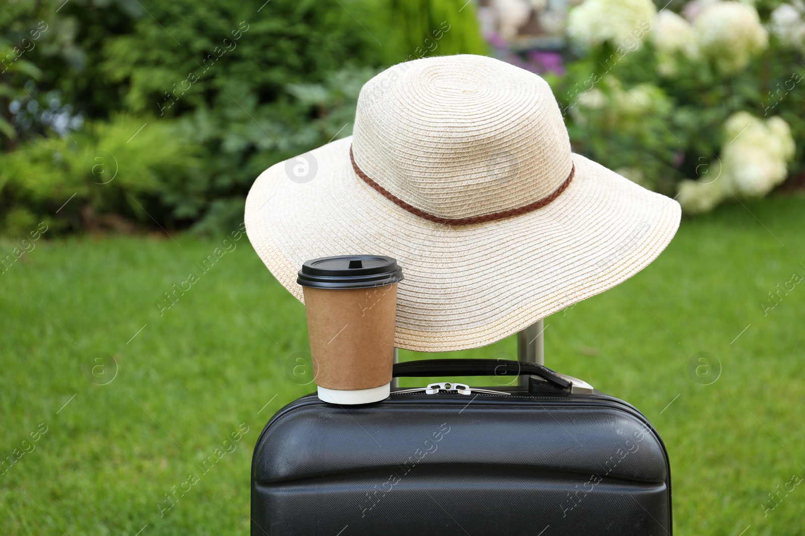 Photo of Paper cup of hot coffee and beige hat on suitcase outdoors. Takeaway drink