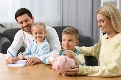 Photo of Planning budget together. Little boy with his family putting coin into piggybank at home