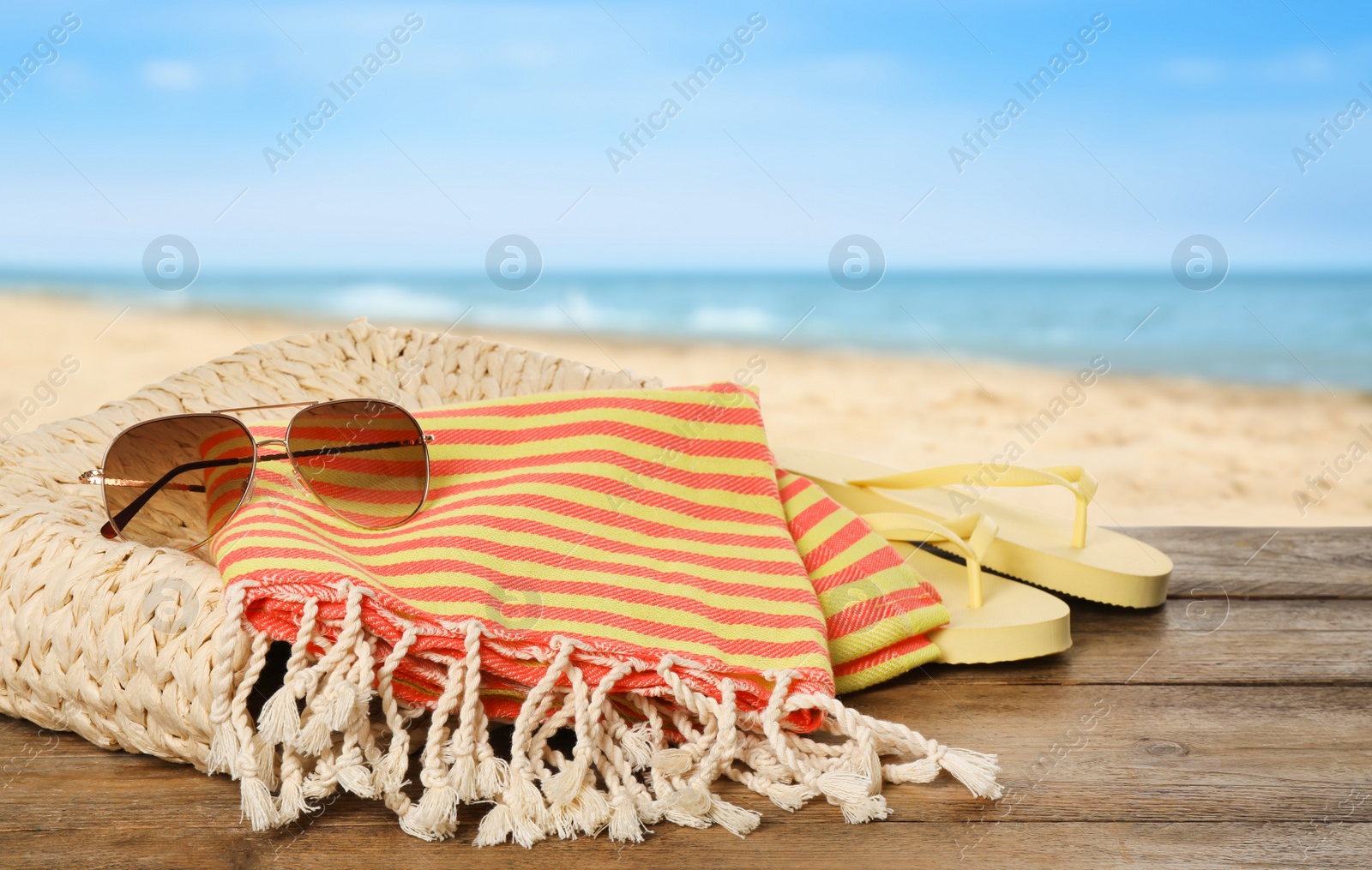 Image of Beach bag with towel, flip flops and sunglasses on wooden surface near seashore
