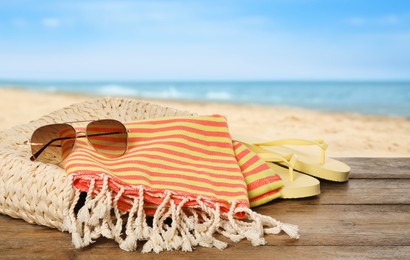 Beach bag with towel, flip flops and sunglasses on wooden surface near seashore