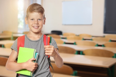 Little boy with school stationery in empty classroom