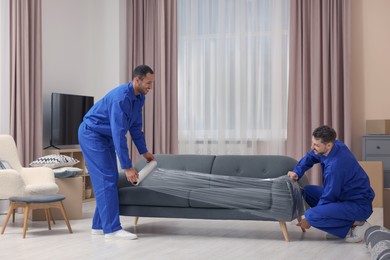 Photo of Male movers with stretch film wrapping sofa in new house