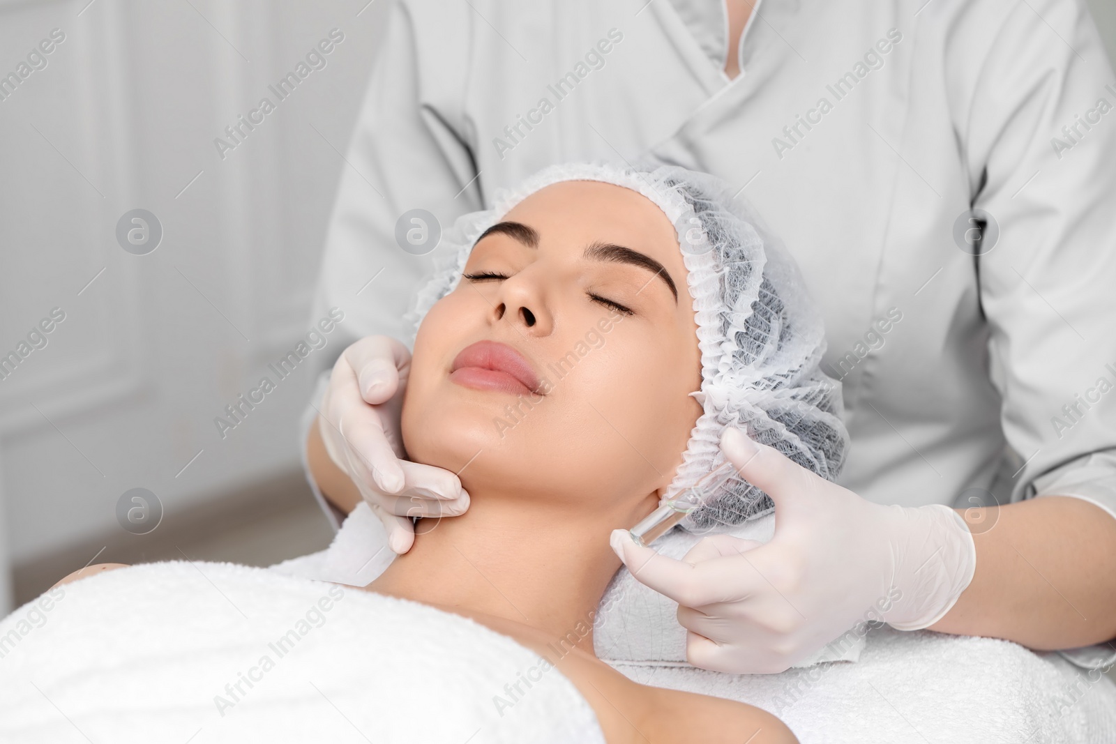 Photo of Professional cosmetologist holding skincare ampoule while working with client in clinic, closeup