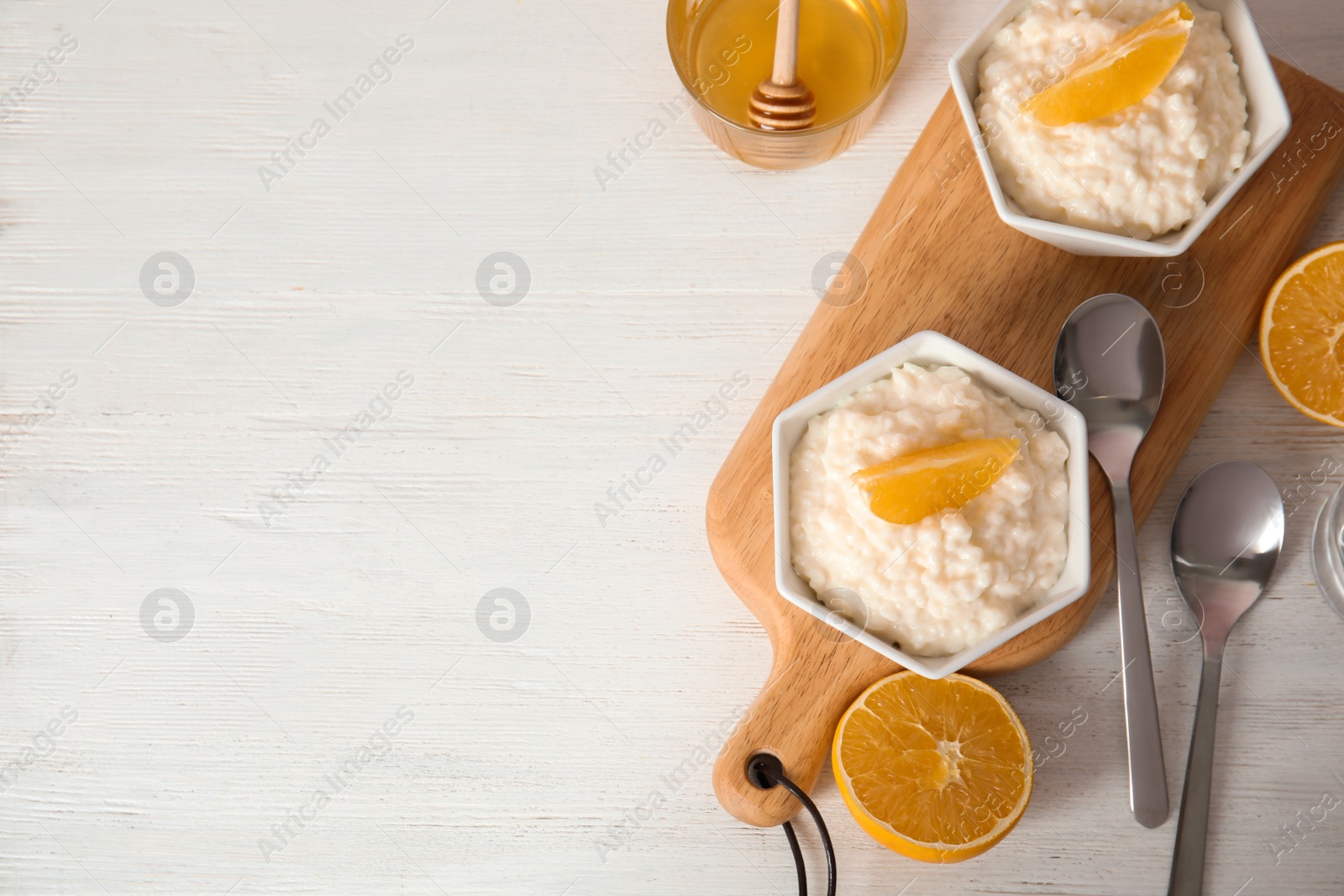 Photo of Creamy rice pudding with orange slices in bowls served on wooden table, top view. Space for text