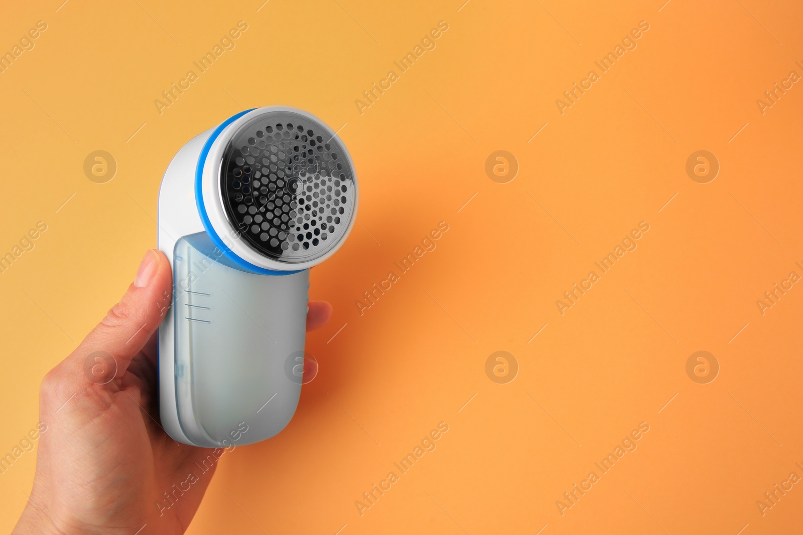 Photo of Woman holding modern fabric shaver on pale orange background, closeup. Space for text