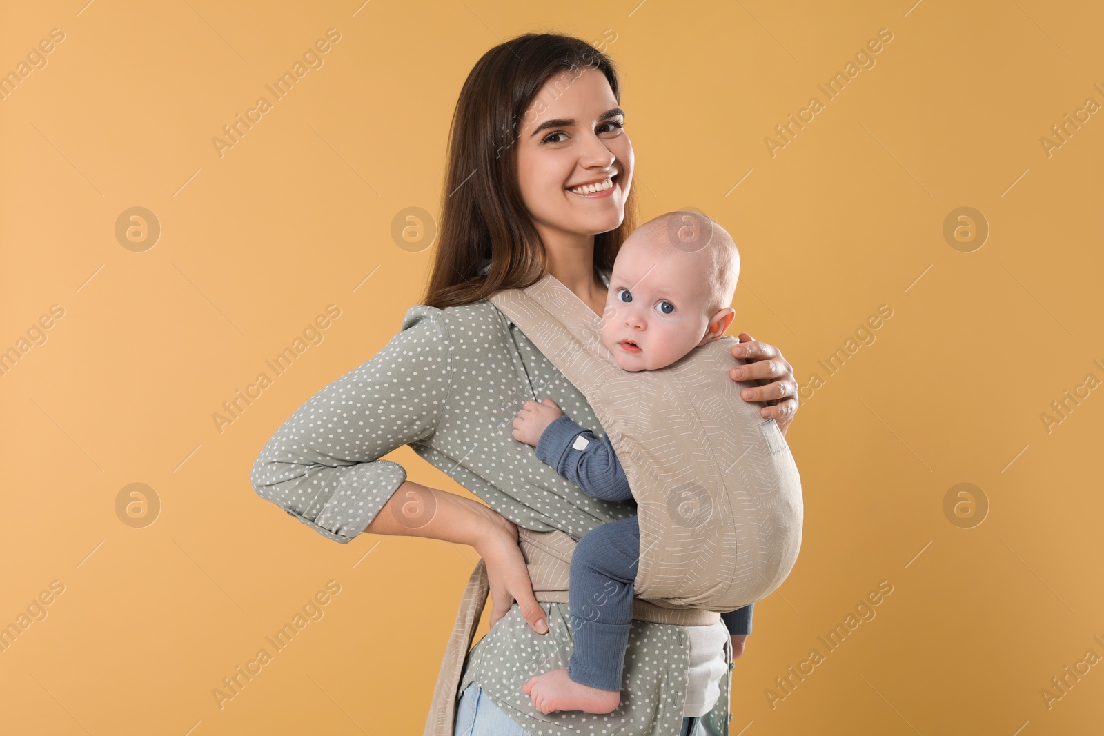 Photo of Mother holding her child in sling (baby carrier) on beige background