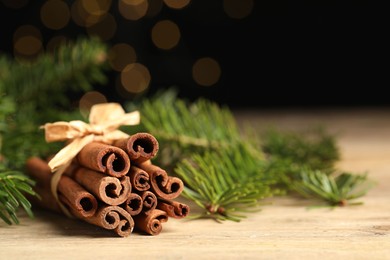 Photo of Bunch of cinnamon sticks and fir branches on wooden table against black background, closeup. Space for text