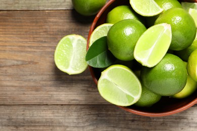 Tasty ripe limes in bowl on wooden table, top view. Space for text