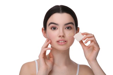 Teenage girl applying foundation on face with makeup sponge against white background