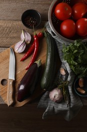 Photo of Cooking ratatouille. Vegetables, peppercorns, herbs and knife on wooden table, flat lay