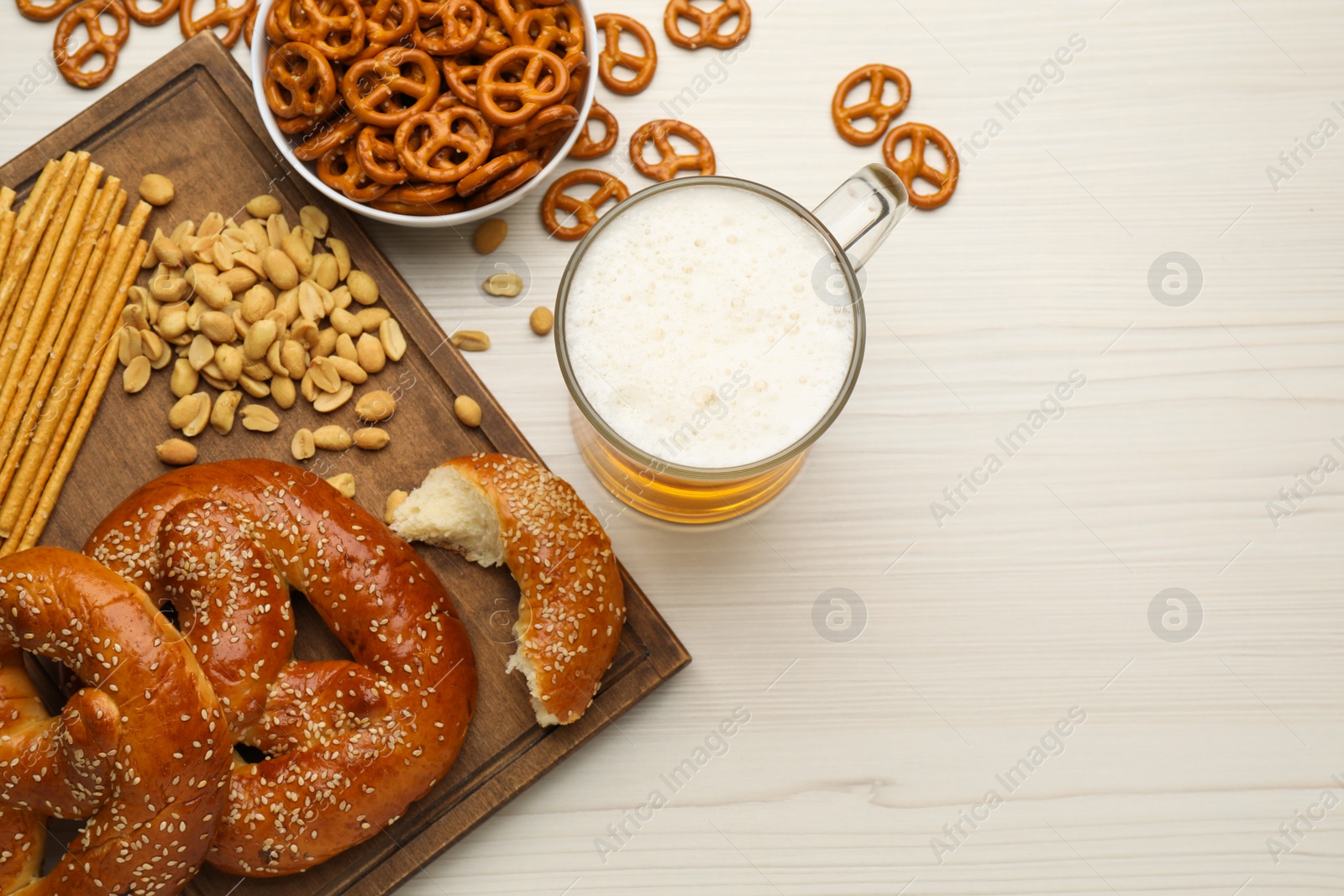 Photo of Glass of beer served with delicious pretzel crackers and other snacks on white wooden table, flat lay. Space for text