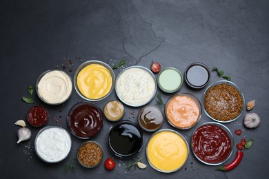 Many different sauces on black table, flat lay