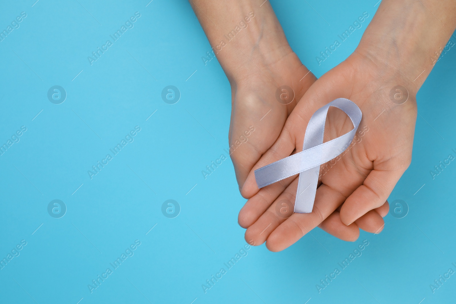 Photo of International Psoriasis Day. Woman with light blue ribbon as symbol of support on light blue background, top view. Space for text