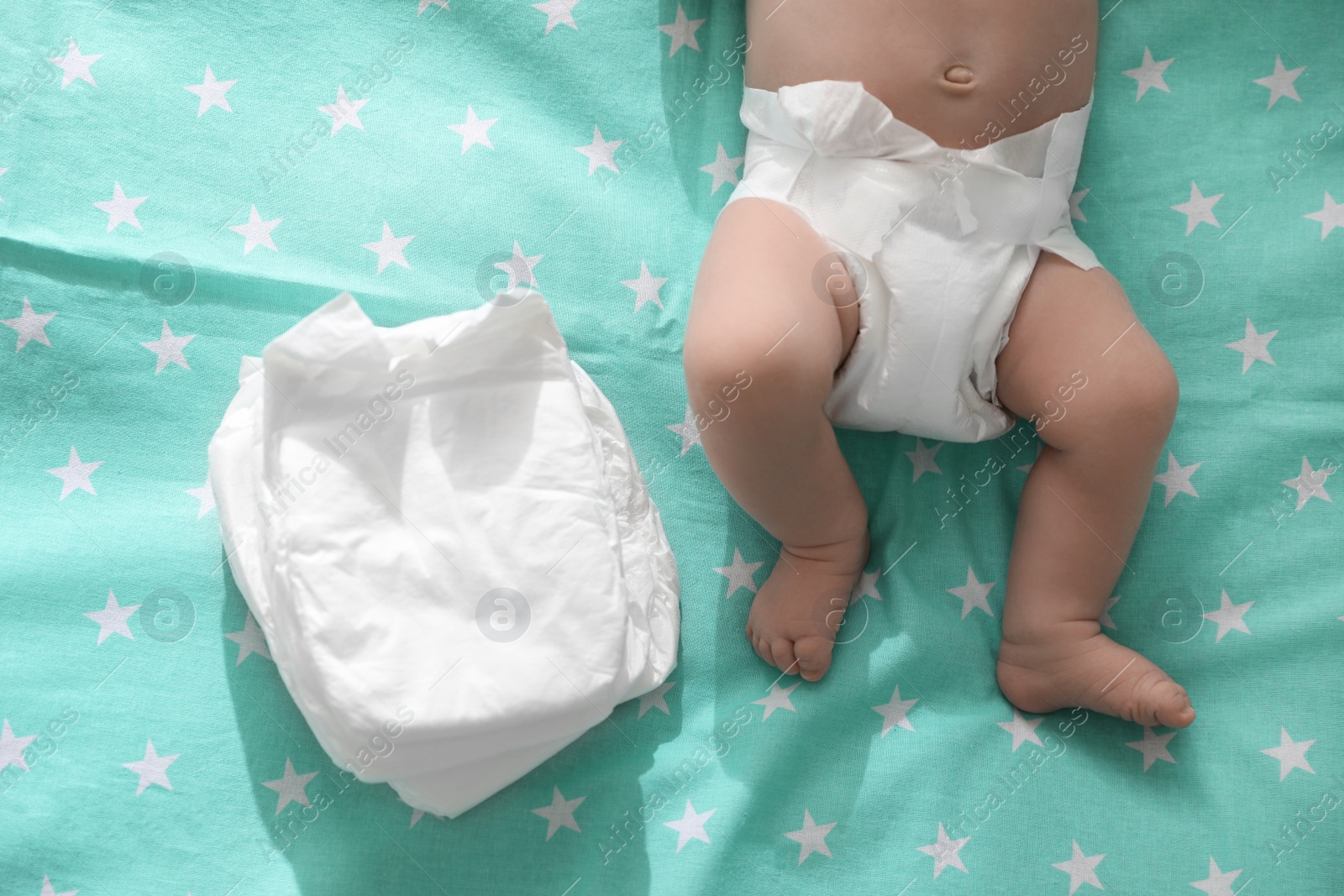 Photo of Cute little baby in diaper lying on bed, top view