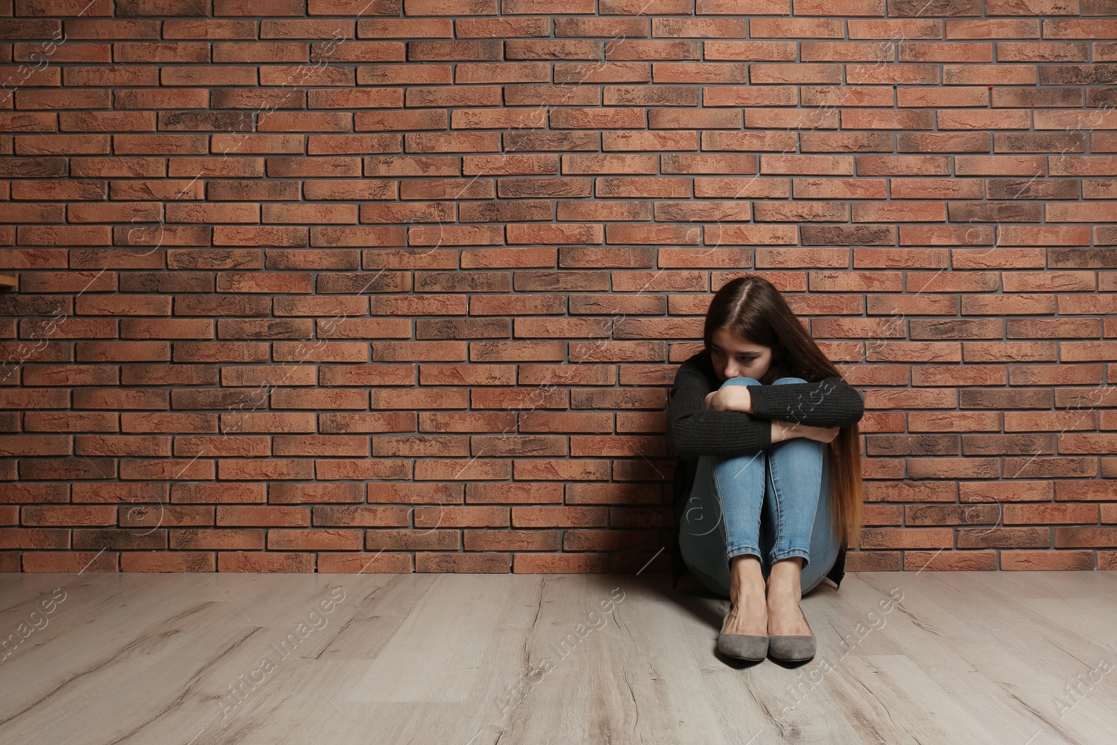 Photo of Upset teenage girl sitting on floor near wall. Space for text