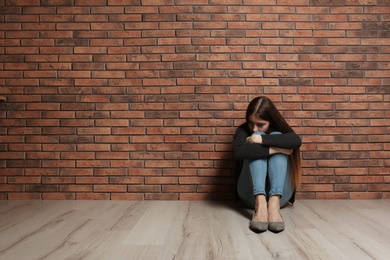 Photo of Upset teenage girl sitting on floor near wall. Space for text