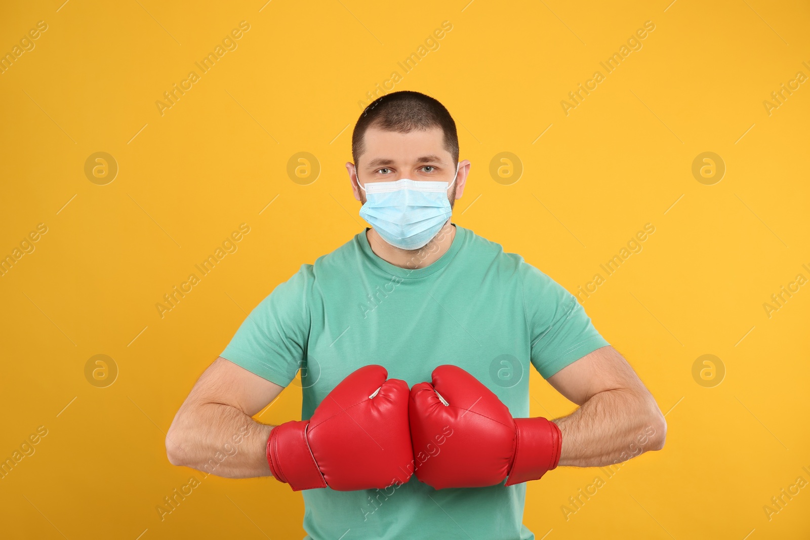 Photo of Man with protective mask and boxing gloves on yellow background. Strong immunity concept