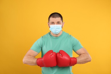 Man with protective mask and boxing gloves on yellow background. Strong immunity concept