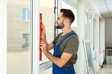 Photo of Construction worker using bubble level while installing window indoors