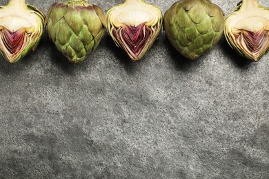 Photo of Cut and whole fresh raw artichokes on grey table, flat lay. Space for text