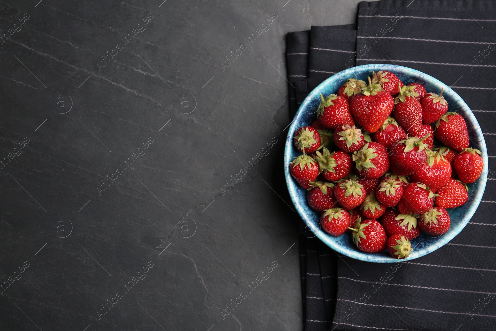 Photo of Delicious ripe strawberries in bowl on black table, flat lay. Space for text