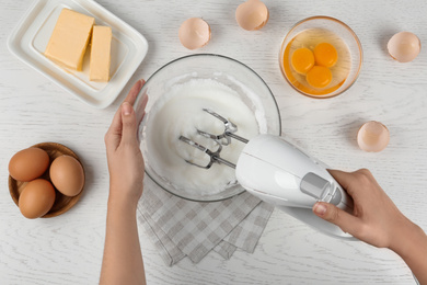 Photo of Woman whipping egg whites at wooden table, top view. Baking pie