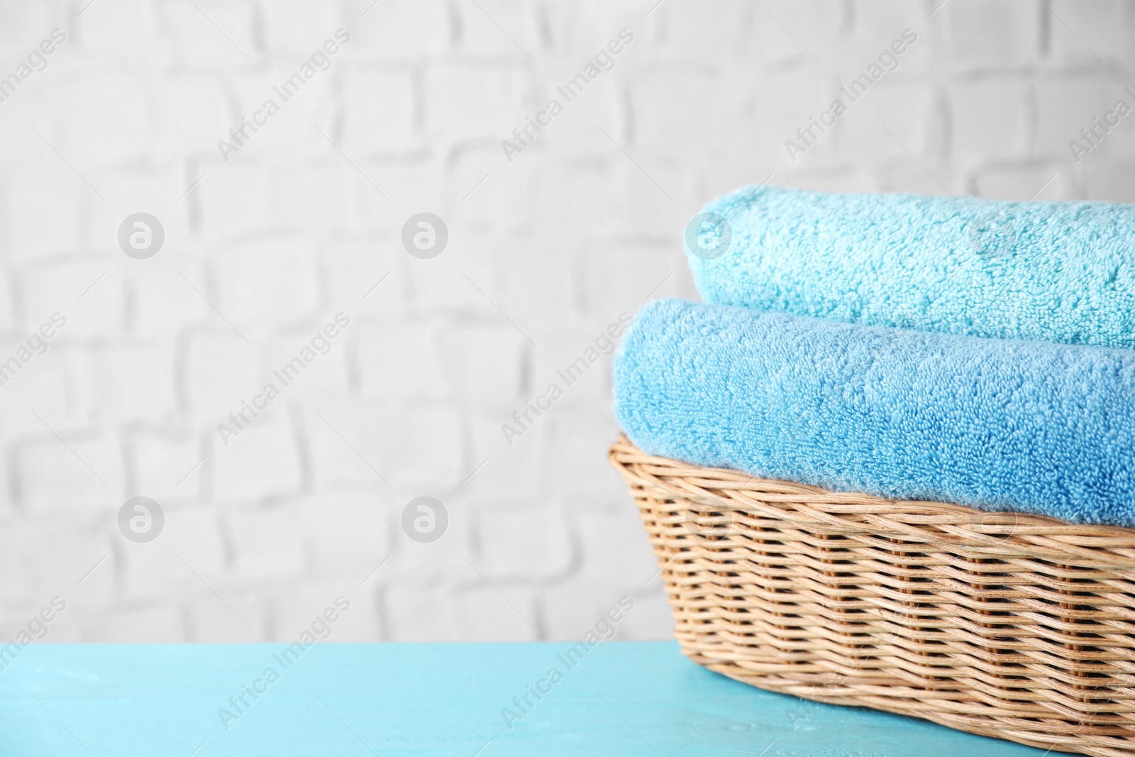 Photo of Wicker basket with clean soft bath towels on blue wooden table. Space for text