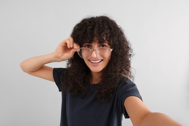 Photo of Beautiful young woman in eyeglasses taking selfie on light grey background