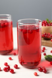 Tasty cranberry juice in glasses and fresh berries on white wooden table, closeup