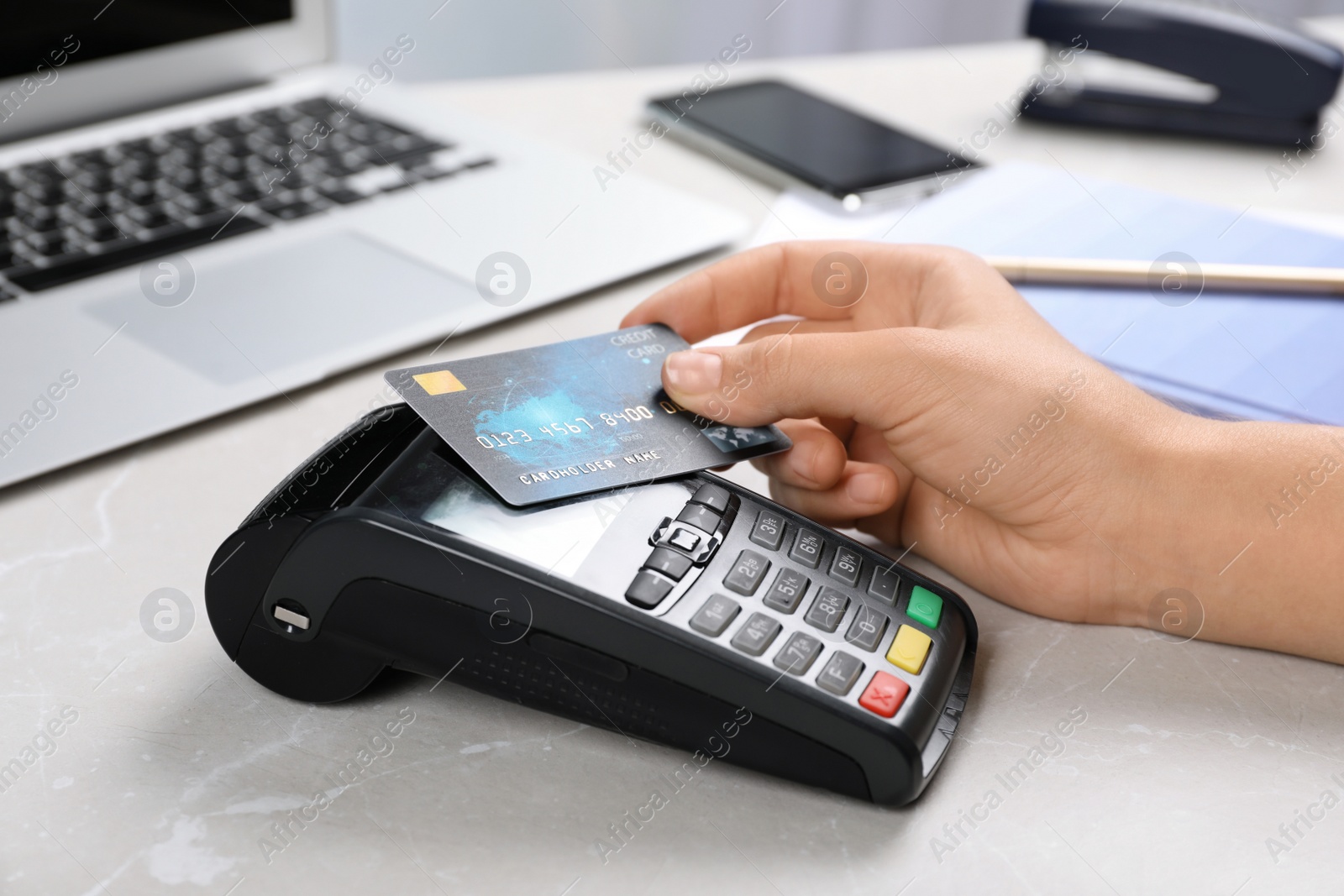 Photo of Woman using terminal for contactless payment with credit card at table