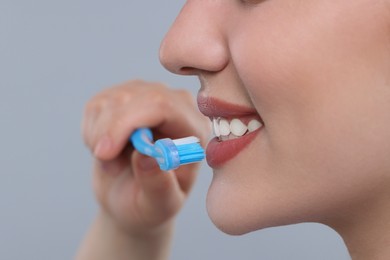 Photo of Woman brushing her teeth with plastic toothbrush on light grey background, closeup. Space for text