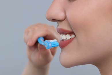 Woman brushing her teeth with plastic toothbrush on light grey background, closeup. Space for text