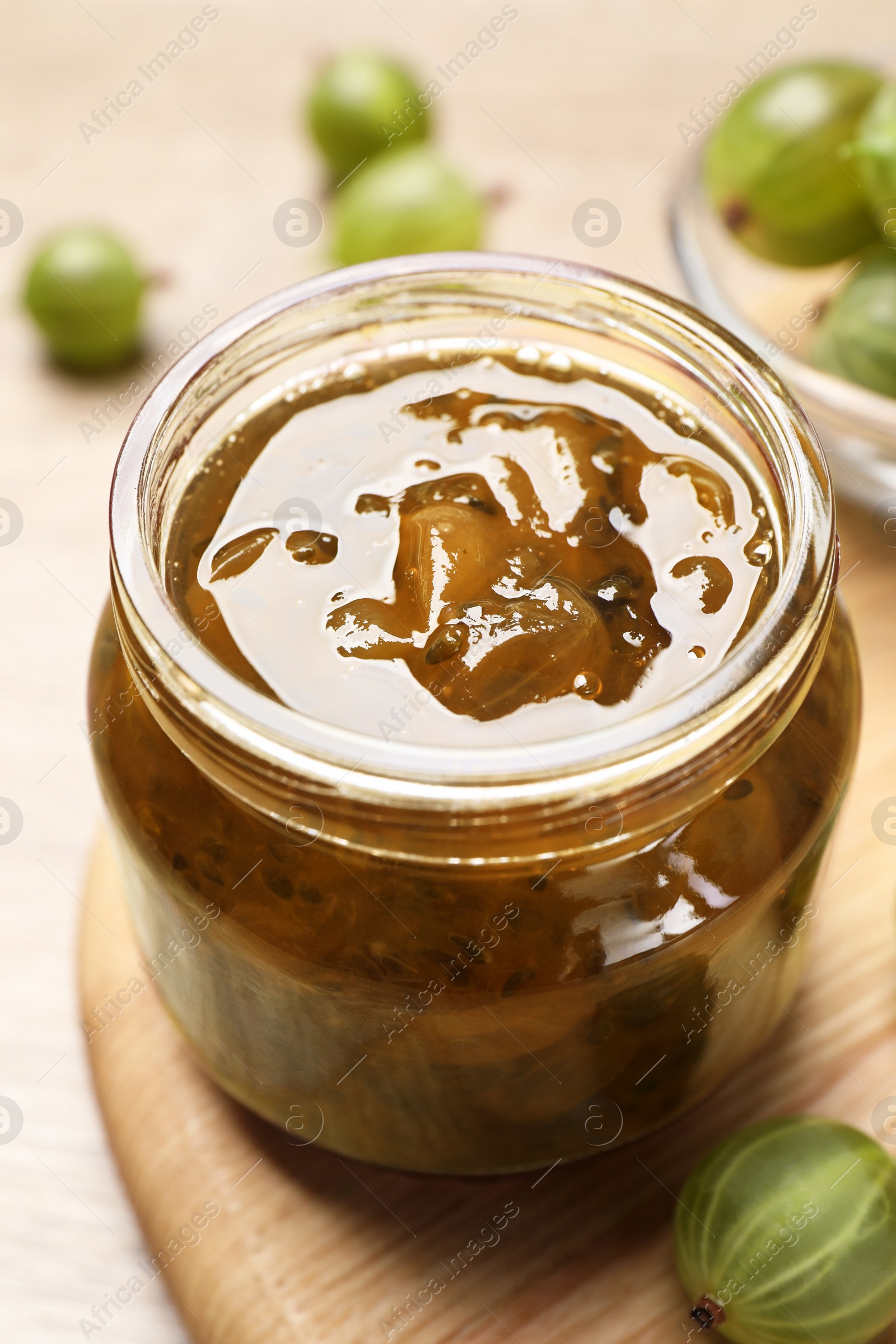 Photo of Jar of delicious gooseberry jam and fresh berries on wooden table, closeup