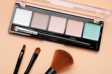 Photo of Colorful contouring palette with brushes on beige background, flat lay. Professional cosmetic product